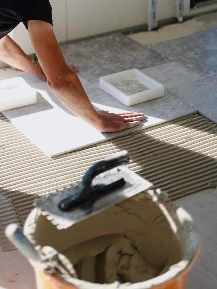 Tradesperson laying floor tiles on site